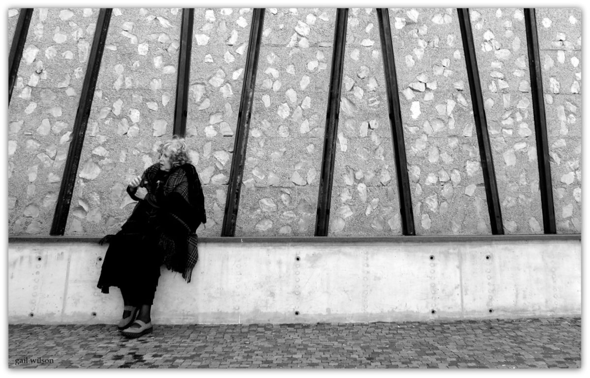 Helen Aron at the Holocaust Museum, Johannesburg, 2019 (photographer Gail Wilson). This photo captures Helen’s mood and sadness in response to the visit to the Museum. Lewis Levin was the architect. Here the exterior façade is clad with “railway lines” and stones embedded in the concrete. Railway lines, transportation to death camps and cattle trucks represented the journeys of so many Holocaust Victims. The railway line images are not straight but are intended to show confusion of genocide. Helen’s parents in the thirties fled to South Africa to give birth to the next generation. 